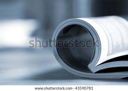 Rolled glossy magazine on a table, with coffee cup behind.  Very shallow depth of field, blue tone.