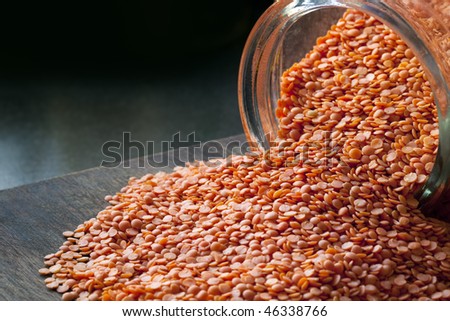 Red lentils spilling from a glass jar onto kitchen board.