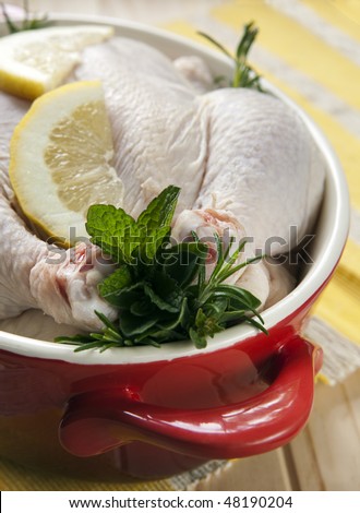 Raw chicken in a red crock pot, stuffed with fresh herbs and lemon, ready for cooking.