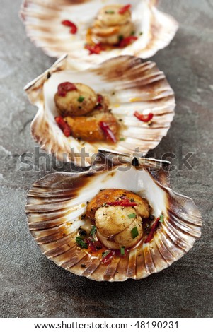 Grilled scallops in scallop shells, with chili.  Focus on front scallop.
