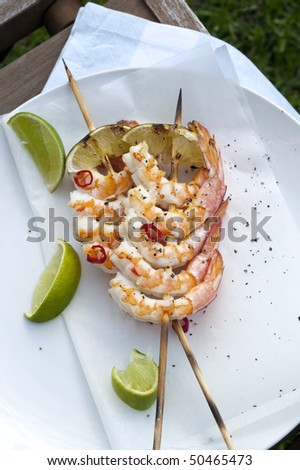Barbecued skewers of king prawns with lime wedges and chili.  Delicious summery seafood.