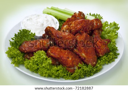 Platter of buffalo wings with a blue cheese dipping sauce and celery sticks.  Hot and spicy!