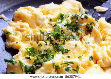 Scrambled eggs cooking in a fry pan, garnished with parsley.