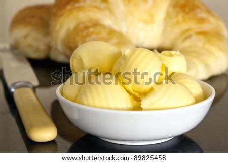 Butter curls in a butter dish, with croissants behind.