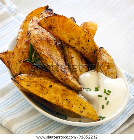 Spicy potato wedges in small bowl with sour cream.