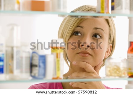 A young woman is looking through her medicine cabinet. Horizontal shot.