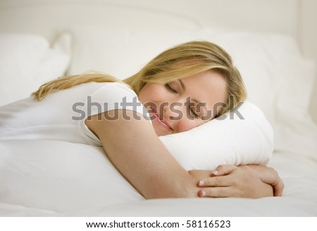 A young woman is lying on her bed with her eyes closed.  She is embracing a pillow.  Horizontal shot.