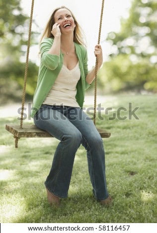 A young woman is sitting on a swing as she talks on her cellphone.  Vertical shot.