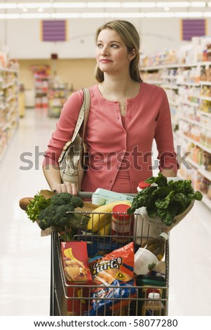 Beautiful young woman walks through a grocery store with a shopping cart full of food.  Vertical shot.