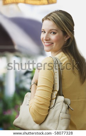 A young woman is smiling over her shoulder at the camera and is carrying a purse.  Vertical shot.