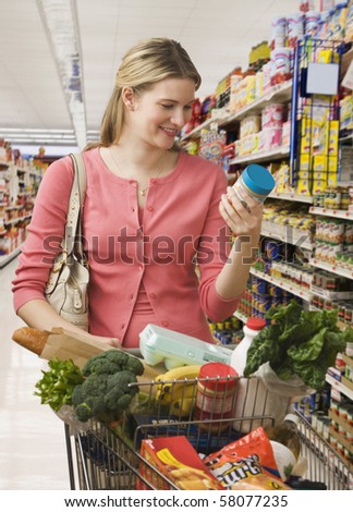 Beautiful young woman reads the label on a jar while shopping at a grocery store.  Vertical shot.