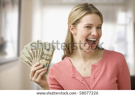 A young woman is holding up cash in a fan and smiling at the camera.  Horizontal shot.