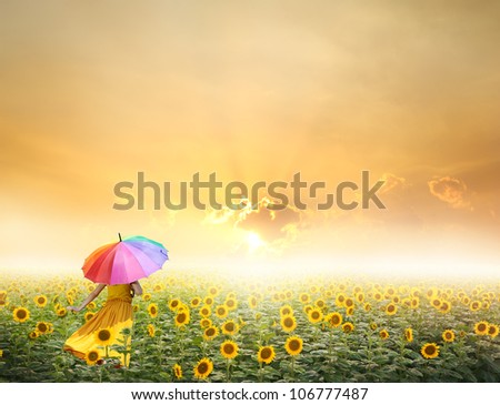 Beautiful woman holding multicolored umbrella in sunflower field and sunset