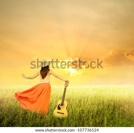 Woman and guitar standing on meadow with sunset