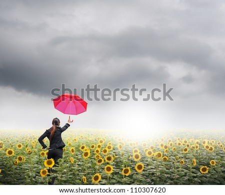 Red umbrella Business woman standing in rainclouds over sunflowers field