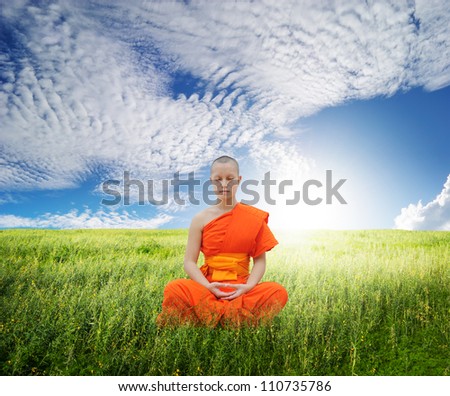 Monk meditating in grass fields and blue sky
