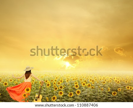 Woman and guitar standing in sunflower fields with sunset