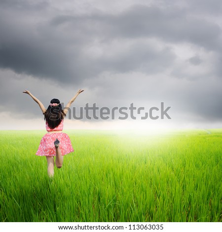 Happy woman jump in green rice fields and rainclouds
