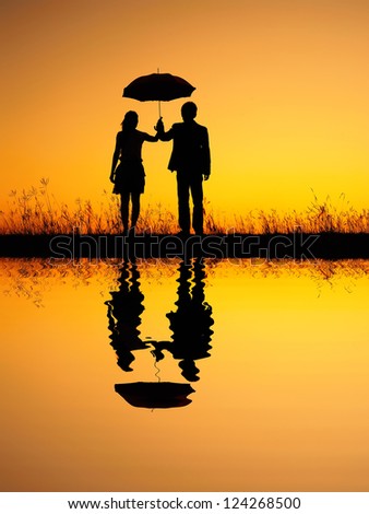 Reflection of Man and woman holding umbrella in evening sunset silhouette