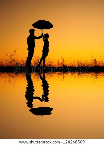 Reflection of Man and woman holding umbrella in evening sunset silhouette