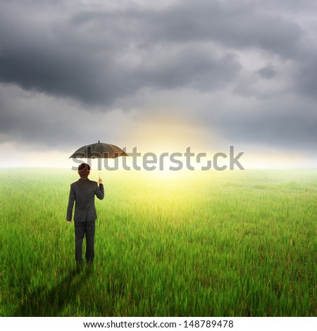Umbrella man standing to raincloud in grassland with umbrella