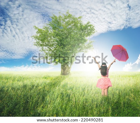 Beautiful woman holding red umbrella and big tree   in green grass field  and cloud sky