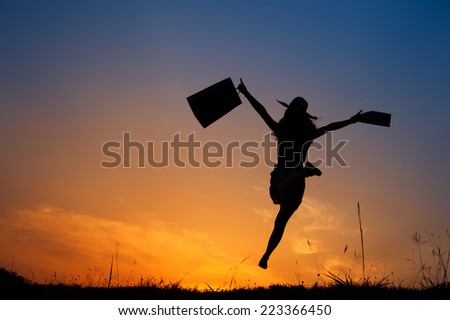 Happy Woman holding shopping bags jumping in sunset silhouette