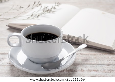 Cup of hot coffee and white note book on wood table background