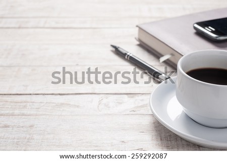 Cup of hot coffee and white note book on wood table background