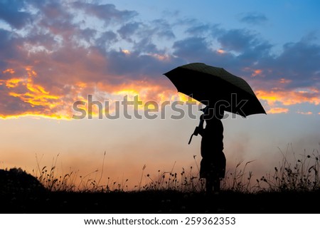 Silhouette of Umbella  boy playing in grass field at sunset