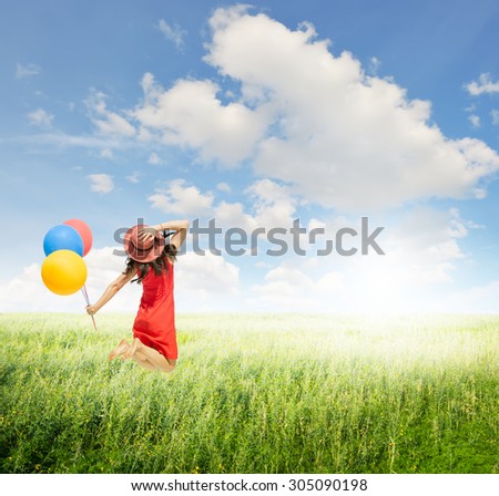 Happy Woman jumping and holding balloons  in green grass fields with clouds sky.Summer holiday concept.