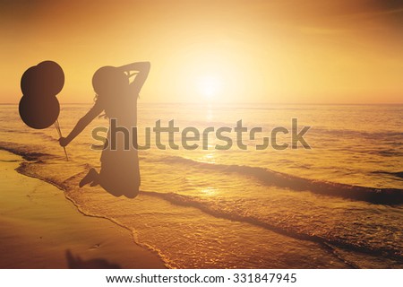 Happy Woman Jumping and holding balloons in Sea beach Sunset silhouette.Copy space