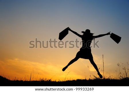 Happy Woman holding shopping bags jumping in sunset silhouette