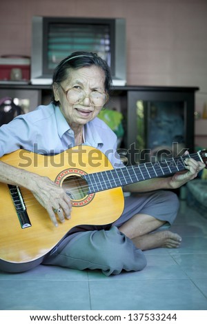 south east asian woman seventy two years old playing guitar