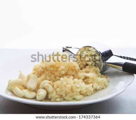 fresh garlic crushed by garlic crusher on white dish on kitchen table top use for food spice and ingredient healthy topic