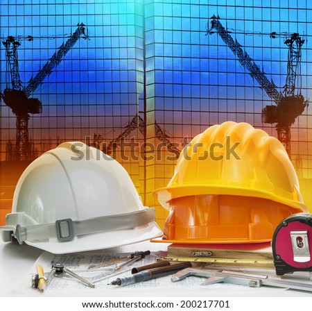 civil engineer working table with safety helmet and writing instrument against beautiful dusky sky and crane construction site