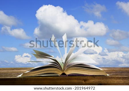 open old book page on wood table with flying book page against beautiful blue sky use for abstract education and idea creative school object