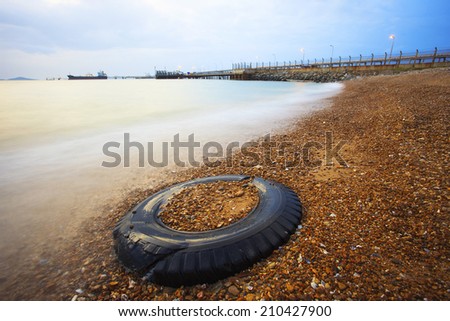 old truck tire on gravel beach against beautiful sea water with long exposure technical photography