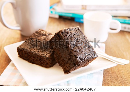 browny cake ready to eat on white dish with coffee cup and magazine book on table top