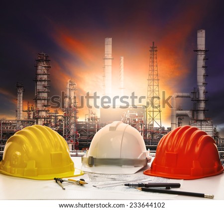 safety helmet on engineer working table against beautiful oil refinery in industry estate