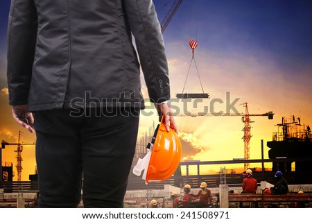 engineering man holding safety helmet and working in building construction site against  structure project site