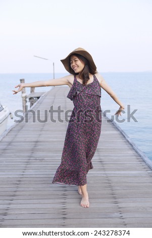 portrait of beautiful young woman wearing wide straw hat and long dress standing with happiness emotion on piers at sea beach