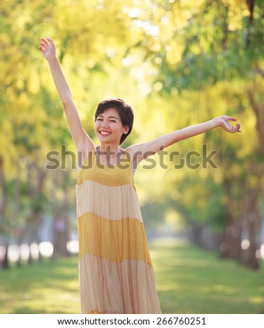 portrait of beautiful young asian woman feeling free with relaxing toothy smile and happy emotion in blur yellow blooming flowers park  background