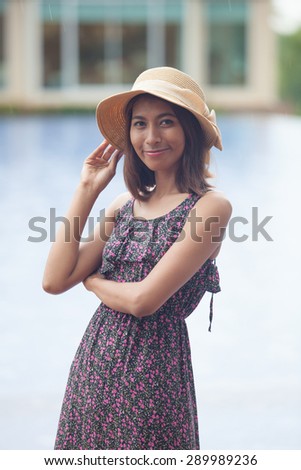 portrait of smiling face of young asian tan skin woman with long dress and fashion wide straw hat standing outdoor in raining day