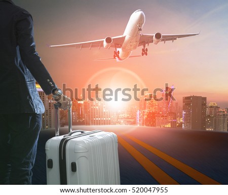 business man and traveling luggage standing against skyline and passenger plane taking over airport runway