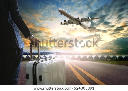 business man and traveling luggage standing in airport terminal and passenger plane flying over sky