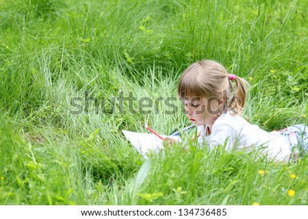 beautiful little girl on the nature draws pencils