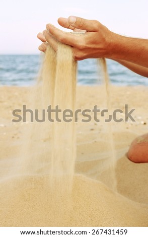 a male hand pours sand on the seashore