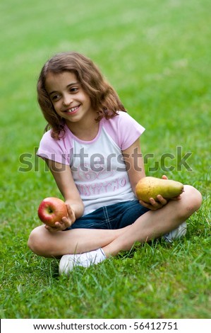 Portrait of a preteen girl with an apple and a plum in her hands and green grass in the background