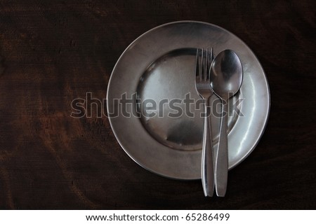 round clean stainless plate with fork spoon on a dark wood table